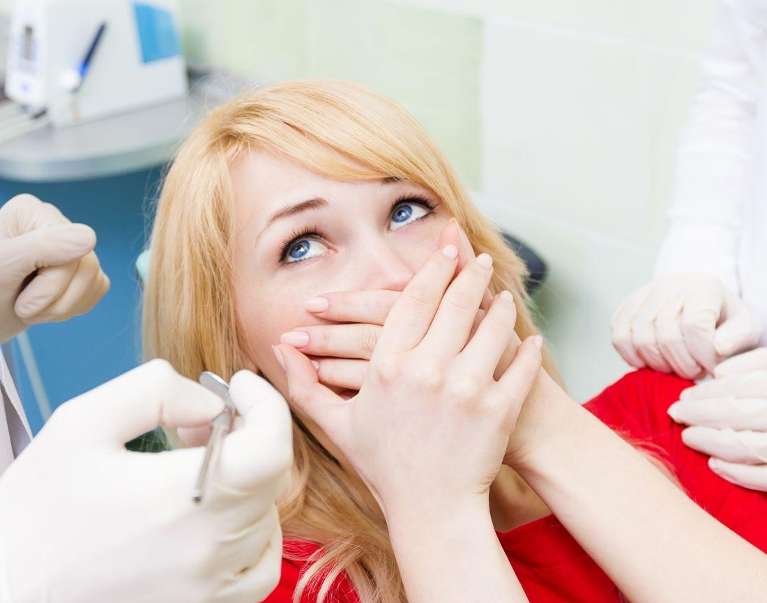 Blonde woman covering her mouth in dental chair, fontana CA